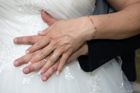wedding couple detail rings fingers bride and groom hands on marriage wed resting on white dress womanの写真素材