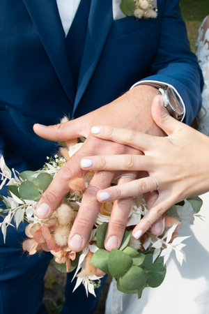 loving marriage bride and groom fingers hands wedding rings close up on bouquet flowersの写真素材