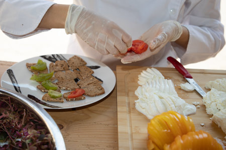 chef preparing food gloved hands placing tomato slices on small appetizer toastsの写真素材
