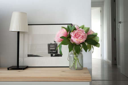 Nordic style auxiliary furniture with a bouquet of peonies, a table lamp and a painting with a black and white photography. Simple and romantic decorationの写真素材