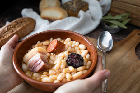 Hands hold a plate of Asturian bean stew ready to eat. Typical dish of the north of Spain. Food photographyの写真素材