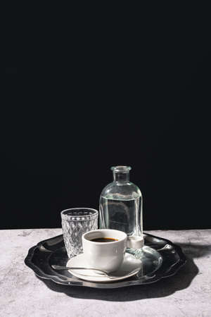 Black coffee with a glass and pitcher of water on an elegant silver tray with a dark backgroundの写真素材