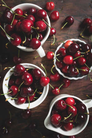 Delicious cherries in white ceramic cups on a wooden table