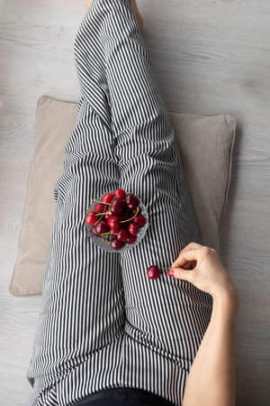 Woman with striped pants and a bowl of red, fresh and ripe cherries