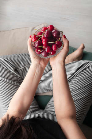 Woman with striped pants and a bowl of red, fresh and ripe cherriesの写真素材