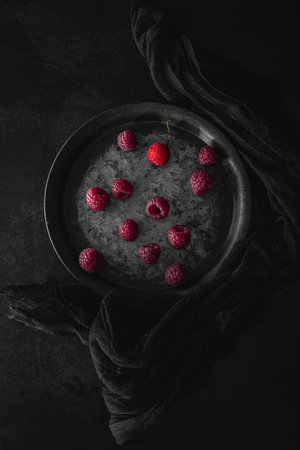 Metallic plate with fresh raspberries. Dark mood food photography with copy spaceの写真素材