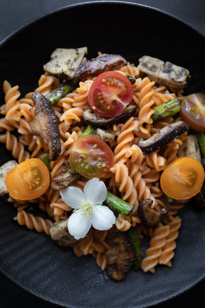 Fusilli pasta with mushrooms, asparagus and cherry tomatoes as closeup on a modern design plateの写真素材