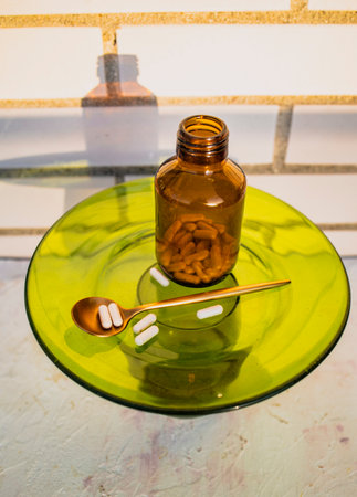 A glass bottle with pills and a spoon on a green glass tableの写真素材
