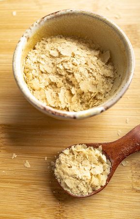 Close-up of a bowl and a wooden spoon with nutritional yeast, excellent vegan protein