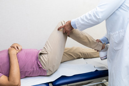 A doctor in a white coat examining a patient's knee during a medical consultation in a clinical setting.の写真素材