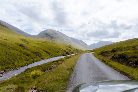A tranquil river winds through the lush, green Glencoe Valley with towering mountains in the background.の写真素材