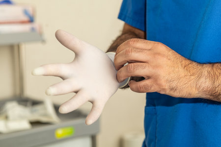 A healthcare professional in blue scrubs putting on surgical gloves, emphasizing hand hygiene and safety in a medical setting.の写真素材