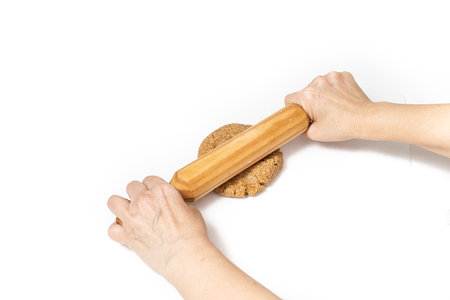 hands kneading homemade oatmeal cookie dough with a rolling pin on a white background with space for textの写真素材