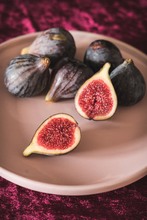 A plate filled with fresh figs sits on a table covered with a luxurious red velvet tablecloth,の写真素材