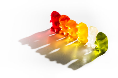 A row of colorful gummy bears arranged on a white background, creating vivid shadowsの写真素材