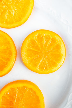 Vibrant candied orange slices displayed on a white ceramic plateの写真素材