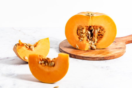 A pumpkin cut into slices on a wooden board, placed on a white kitchen counterの写真素材