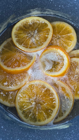 orange slices gently caramelizing in a saucepan filled with bubbling water and sugar, creating a mesmerizing view of the cooking process for desserts or garnishes.の写真素材