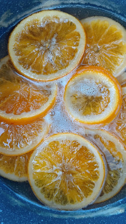 orange slices gently caramelizing in a saucepan filled with bubbling water and sugar, creating a mesmerizing view of the cooking process for desserts or garnishes.の写真素材