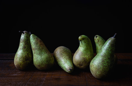 Six ripe conference pears arranged on a wooden table, contrasting beautifully against a dark background for a rustic and elegant lookの写真素材