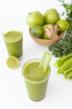 Refreshing green detox juice made with kale, celery, lemon, ginger, and green apple, placed on a white kitchen counter with natural lightingの写真素材