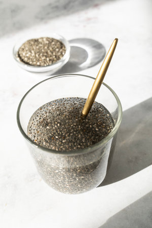 dry chia seeds in a bowl next to a glass of soaked chia seeds releasing their natural gel.の写真素材