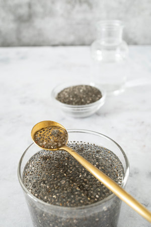 A top view of dry chia seeds in a bowl next to a glass of soaked chia seeds releasing their natural gelの写真素材