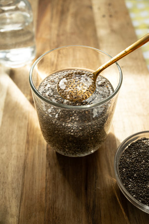 A warm and natural scene showing chia seeds in a glass of water with a golden spoon. The seeds are releasing their gel-like mucilage, highlighting their transformation into a nutrient-rich superfood.の写真素材