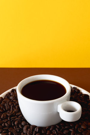 Stylized coffee scene featuring a white ceramic cup filled with black coffee and roasted beans placed on a solid colored background.の写真素材