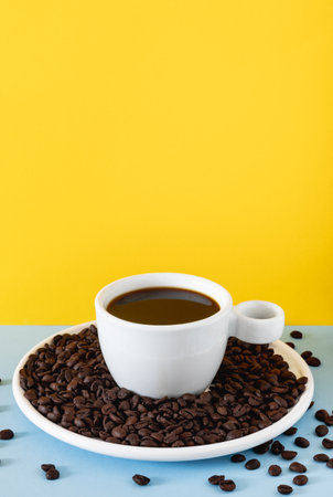 Stylized coffee scene featuring a white ceramic cup filled with black coffee and roasted beans placed on a solid colored background.の写真素材