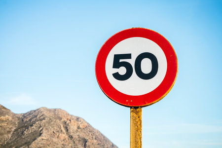 A clear and simple image of a round 50 speed limit traffic sign placed against a bright sky blue...