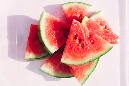 Top view of freshly cut watermelon slices arranged on a soft pastel pink background.の写真素材