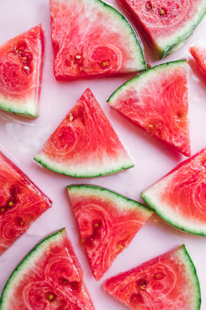 Top view of freshly cut watermelon slices arranged on a soft pastel pink background.