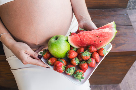 Young pregnant woman holding a plate with fresh seasonal fruitsの写真素材