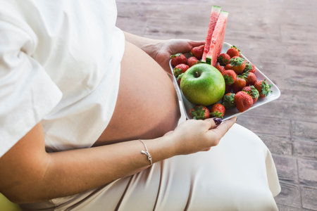 Young pregnant woman holding a plate with fresh seasonal fruitsの写真素材
