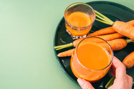 Green plate with two clear glasses filled with freshly squeezed carrot juice, ready to drink.の写真素材