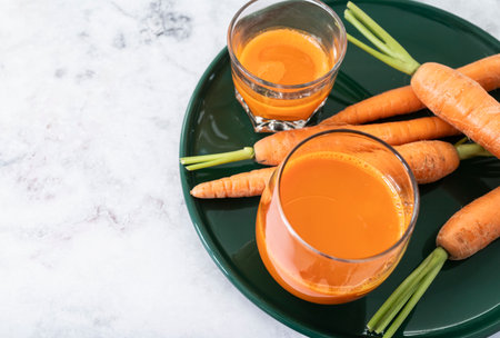 Green plate with two clear glasses filled with freshly squeezed carrot juice, ready to drink.の写真素材