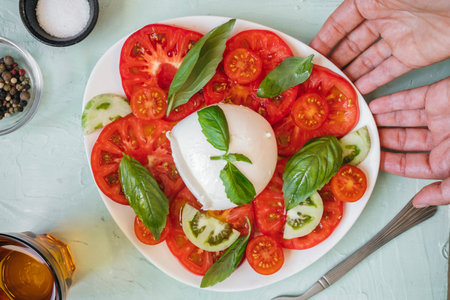Traditional Italian Caprese salad with fresh tomatoes, mozzarella cheese, basil leaves, and olive...