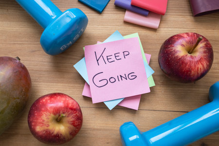 Green sticky note with handwritten â€œKeep Goingâ€ message placed on a table surrounded by...