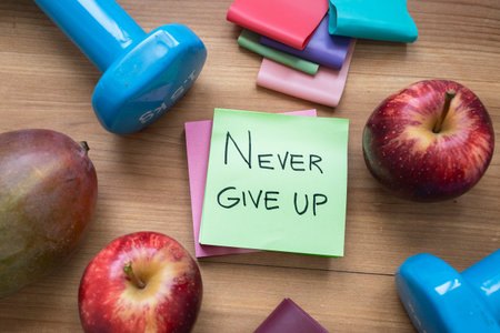 Green sticky note with handwritten â€œNever Give Upâ€ message placed on a table surrounded...