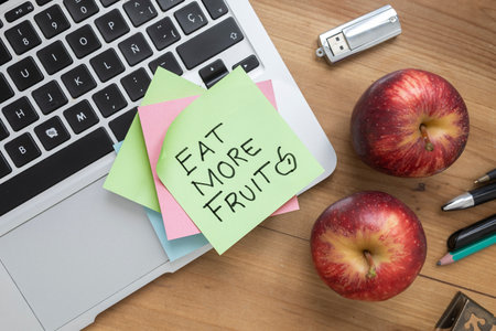 Green sticky note with handwritten â€œEat More Fruitâ€ message placed on a laptop keyboard,...