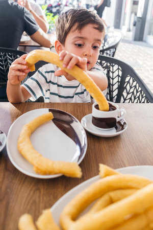 Child enjoying a snack of churros with a cup of thick hot chocolateの写真素材