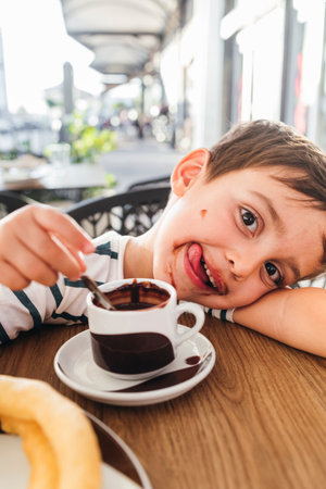 Smiling child enjoying a cup of hot chocolate with churros.の写真素材