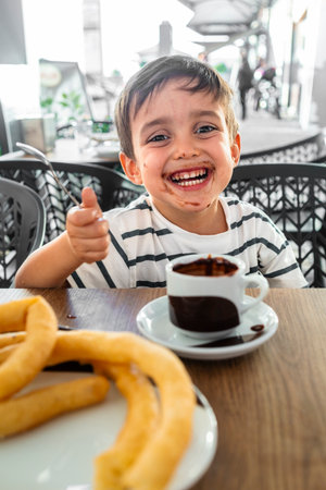Smiling child enjoying a cup of hot chocolate with churros.の写真素材