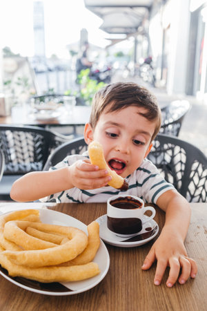 Child enjoying a snack of churros with a cup of thick hot chocolateの写真素材