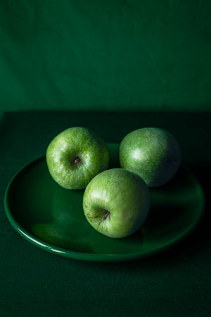 Fresh green apples arranged on a plate with a matching green backgroundの写真素材