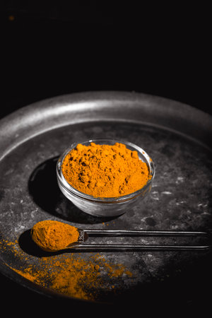 Golden turmeric powder served on a dark plate over a contrasting background.の写真素材