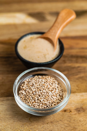 Two small glass bowls, one filled with sesame seeds and the other with creamy tahini paste.