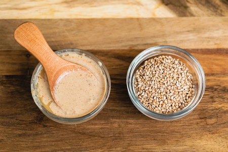 Two small glass bowls, one filled with sesame seeds and the other with creamy tahini paste.の写真素材