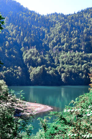 Beautiful blue clear emerald lake glowing in the sun near green trees high in Abkhazian mountainsの写真素材